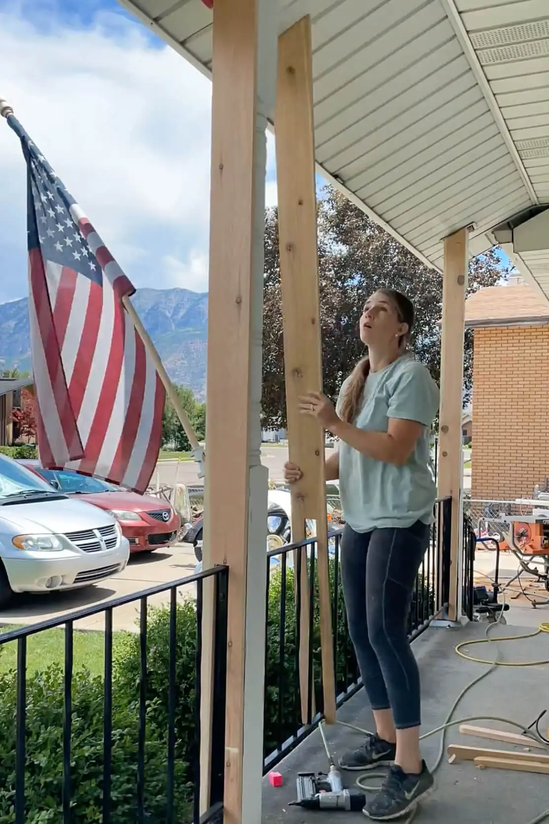 Woman aligning and securing a wooden wrap over an old front porch post as part of a budget-friendly DIY curb appeal project.